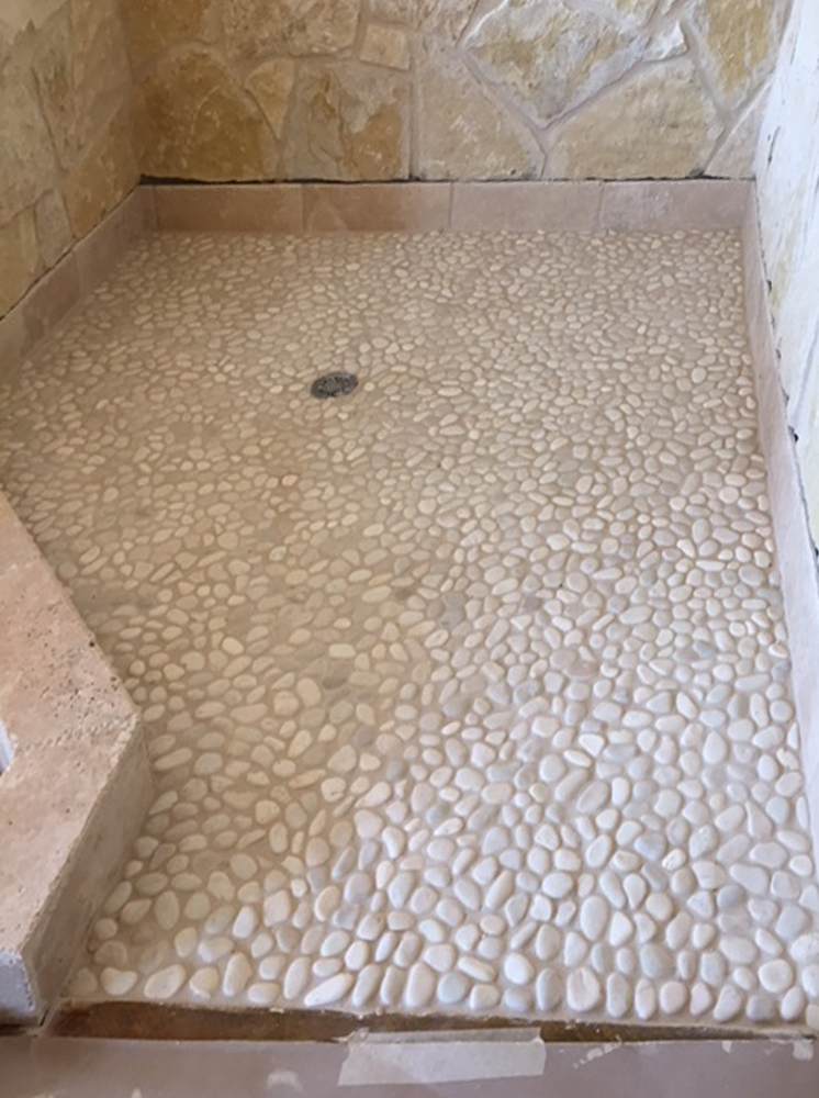white pebble tile shower pan with stone walls